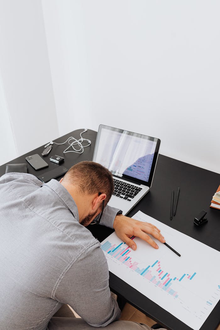 Exhausted man asleep on desk surrounded by work items, depicting stress.